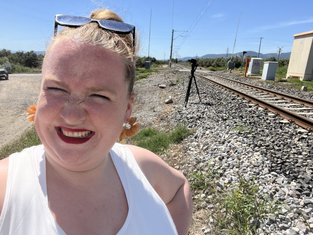 Ella stands in the foreground next to the train tracks in Turkey behind her left shoulder is a camera and tripod pointing at the tracks.