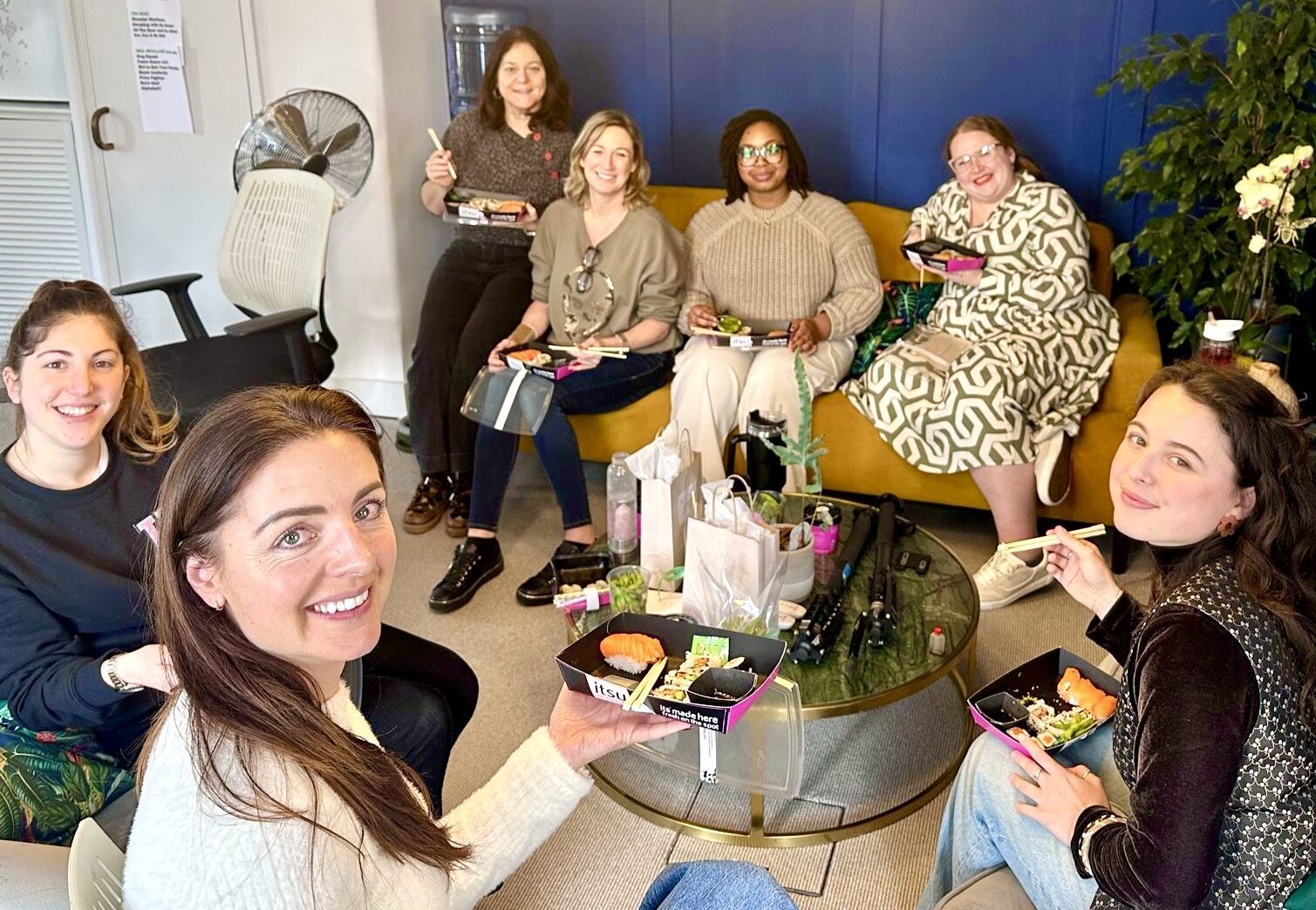 All the women from the spark office sit around on sofas enjoying a sushi lunch for international women's day